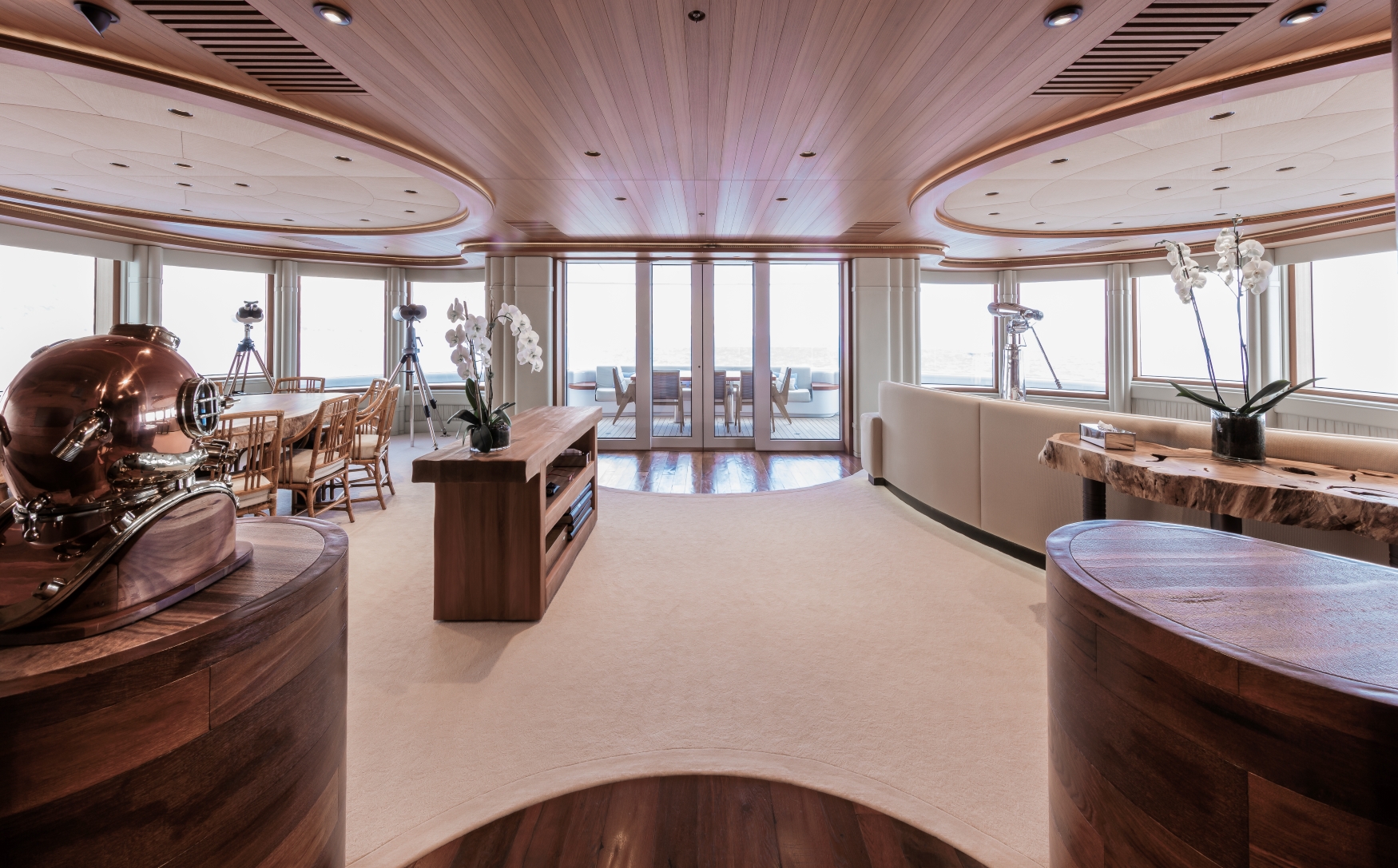 Original yacht saloon photograph with curved wood cabinetry, orchids and panoramic windows overlooking the aft deck.